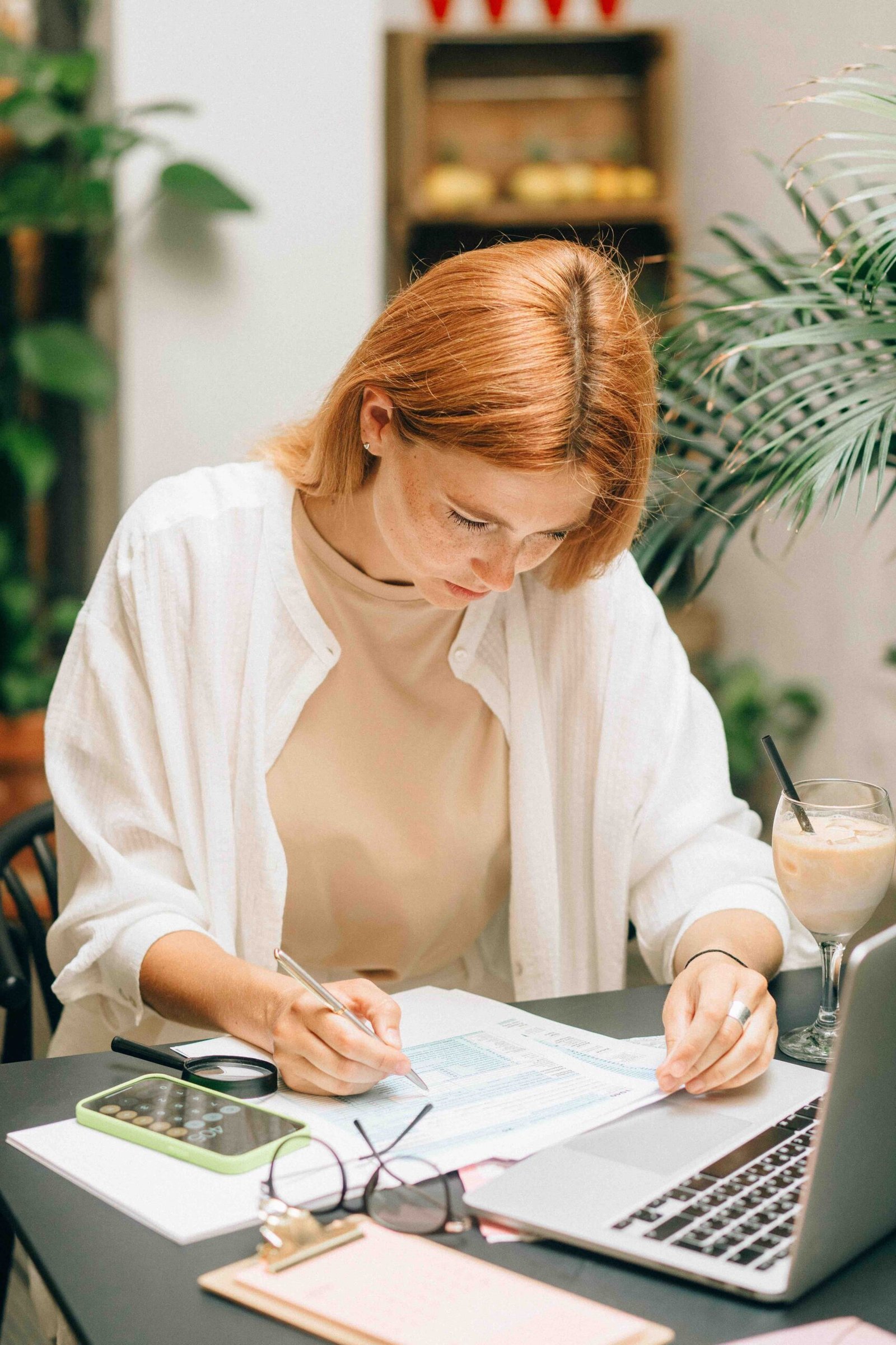 Business woman sitting at her desk, in front of her laptop and going through a list of unpaid invoices with a highlighter pen