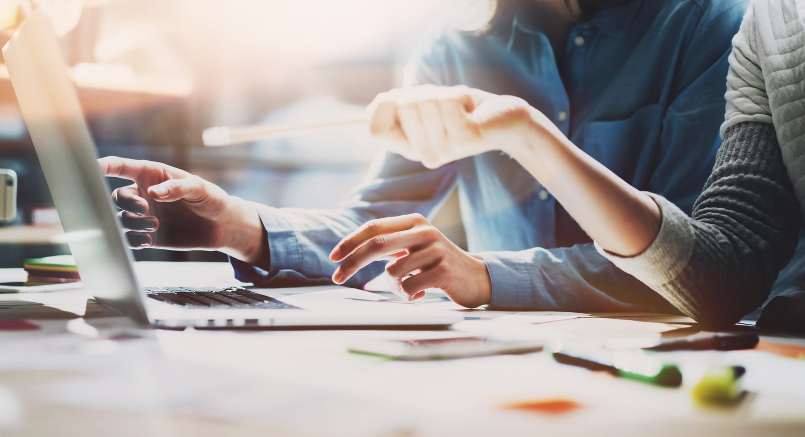 hands of two creatives are pointing at a laptop screen as though they are discussing the best way forward